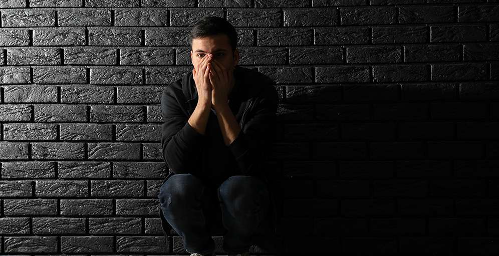 Man in despair leaning against wall.