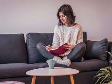 Woman journaling on a sofa while reflecting on the Adaptive Information Processing (AIP) model
