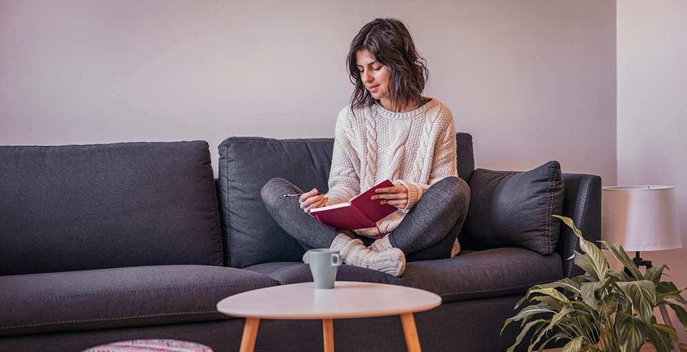Woman journaling on a sofa while reflecting on the Adaptive Information Processing (AIP) model